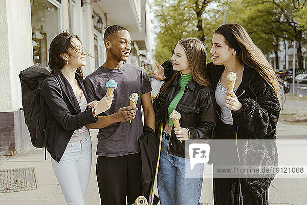 Happy young friends eating ice creams at sidewalk