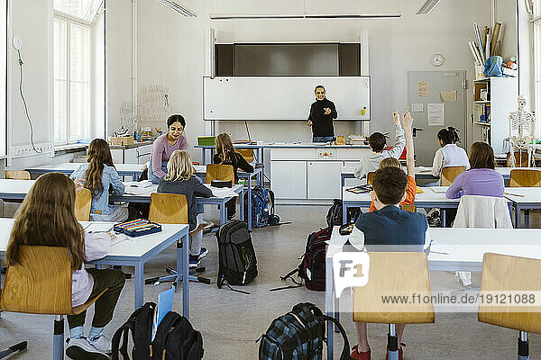 Männlicher und weiblicher Lehrer unterrichten Schüler  die auf einer Bank im Klassenzimmer sitzen
