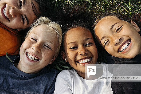 Porträt von fröhlichen Kindern  die im Sommerlager zusammen im Gras liegen