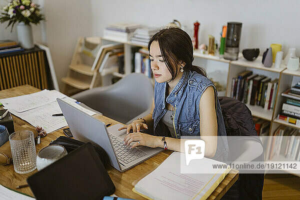 Junge Frau  die einen Laptop benutzt  während sie eine Schulaufgabe zu Hause erledigt