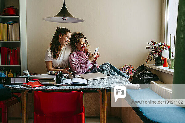 Glückliche junge Freundinnen teilen sich ein Smartphone  während sie zu Hause sitzen