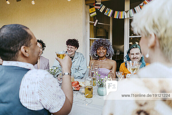 Lächelnde Freunde der LGBTQ-Gemeinschaft genießen Wein bei einer Dinnerparty im Hinterhof