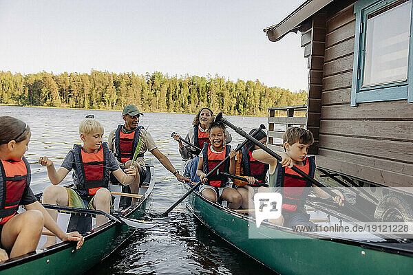 Kids holding oars while sitting in kayaks with counselors on lake at summer camp
