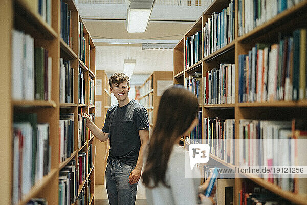 Zufriedene Studenten  die in der Bibliothek der Universität Bücher im Regal suchen
