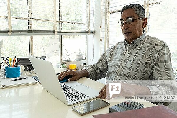 Älterer hispanischer Mann  der einen Laptop für geschäftliche Zwecke benutzt. Textfreiraum