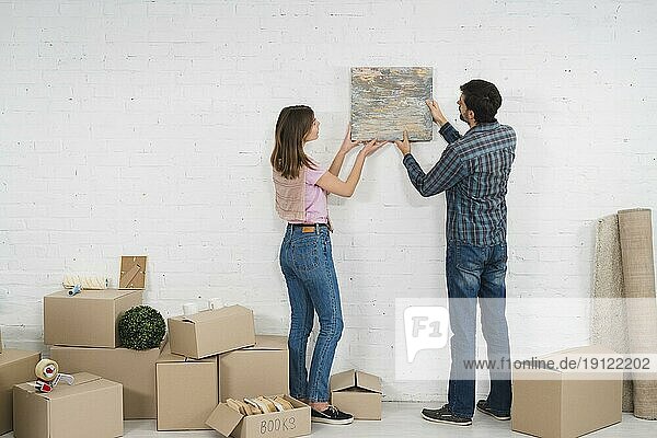 Rückansicht junges Paar platziert Bilderrahmen weiße Wand mit Pappkartons