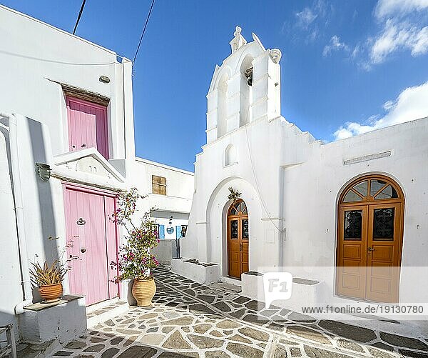 White Greek Orthodox Church  White Cycladic houses with pink doors and windows and flower pots  picturesque alleys of the village of Marpissa  Paros  Cyclades  Greece  Europe