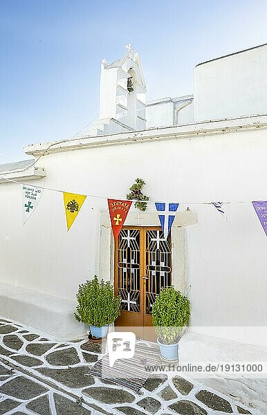 White Greek Orthodox church with colourful flags  picturesque alleys of the village of Marpissa  Paros  Cyclades  Greece  Europe