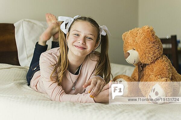 Smiling young woman lying bed with teddy bear