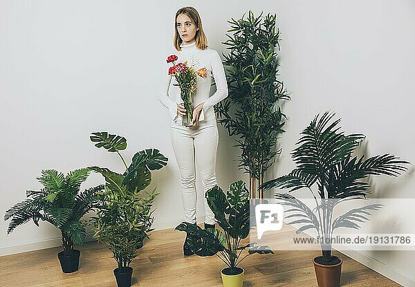 Nachdenkliche Frau mit Blumenvase neben Grünpflanze