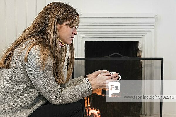Frau Pullover trinkt Tee am Kamin