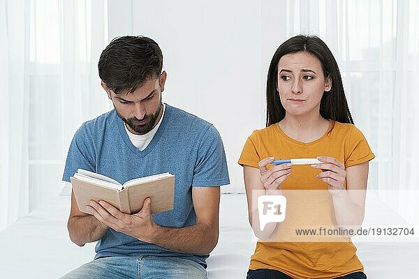Besorgte Frau hält Schwangerschaftstest mit Mann  der liest