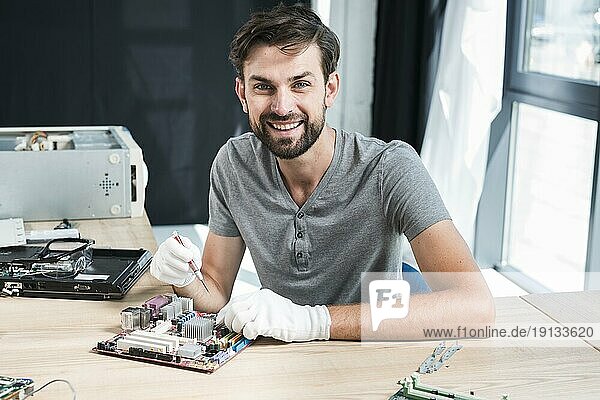 Porträt lächelnder männlicher Techniker bei der Arbeit an einem Computermotherboard