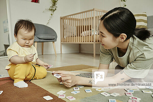 Mother playing word puzzle with daughter sitting on carpet at home