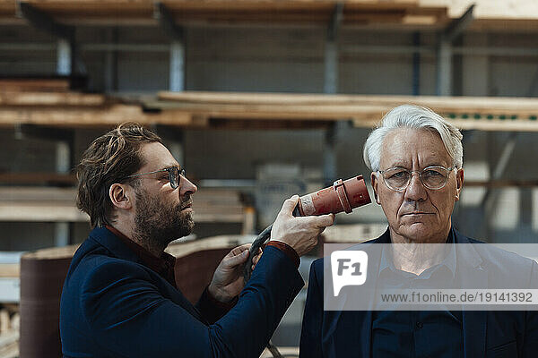 Businessman holding electricity cable near colleague's ear in industry