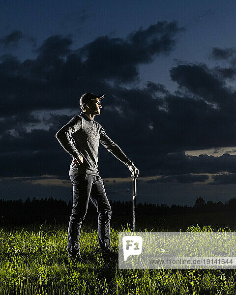 Man with hand on hip standing on grass holding golf club