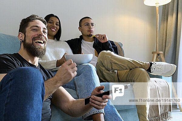 Cheerful friends spending leisure time watching TV at home