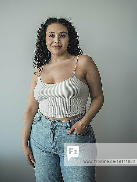 Curvy woman with hand in pocket standing in front of wall