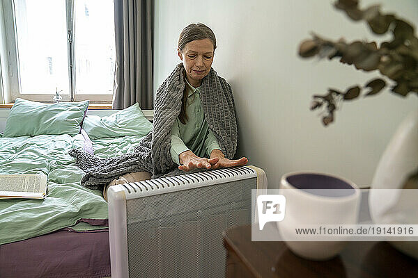 Mature woman warming hands on radiator at home