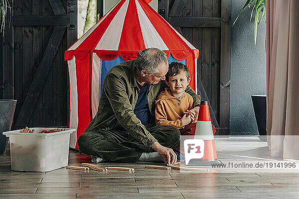 Grandfather embracing grandson sitting near tent at home