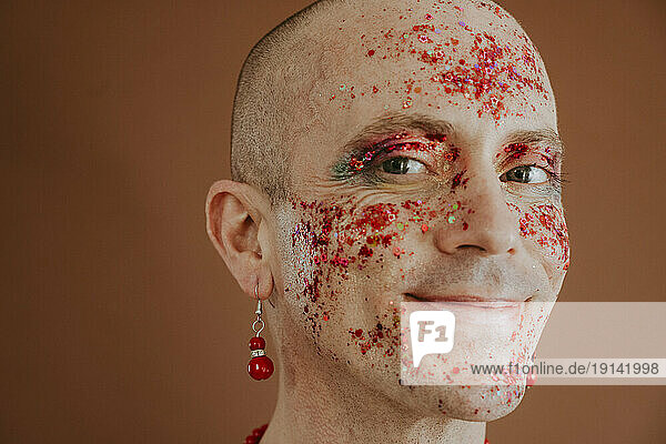 Smiling face of drag queen with red glitter on face against brown background