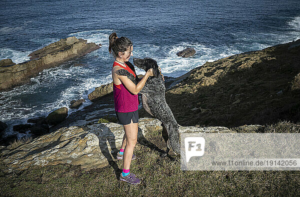 Woman standing with dog on rocks near sea