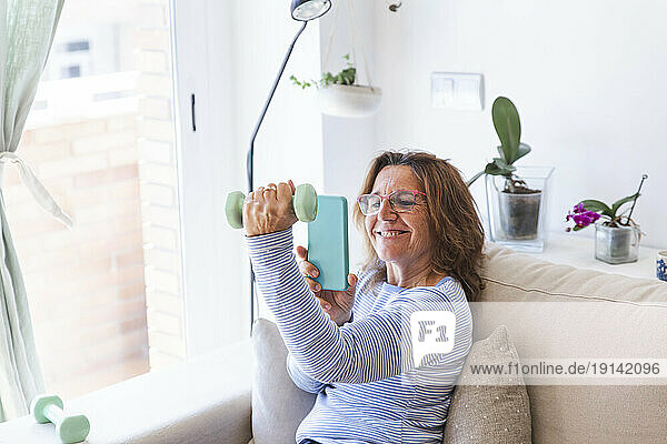 Woman taking picture of hand holding dumbbell through smart phone at home