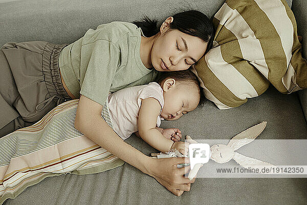 Mother and daughter sleeping together on sofa at home