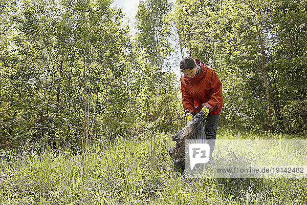 Volunteer collecting garbage on grass at forest