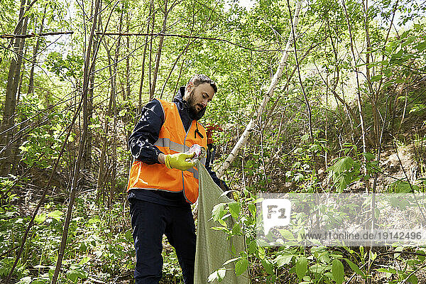 Volunteer collecting garbage amidst plants in forest