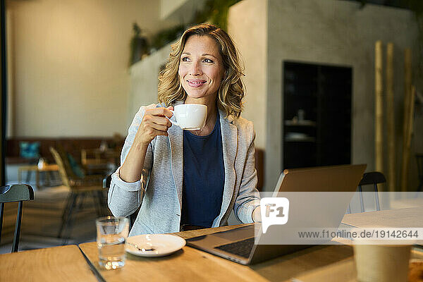 Smiling businesswoman having coffee sitting with laptop at cafe