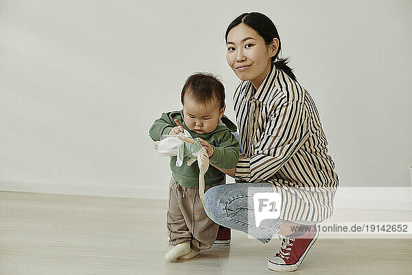 Smiling woman crouching with daughter in front of wall