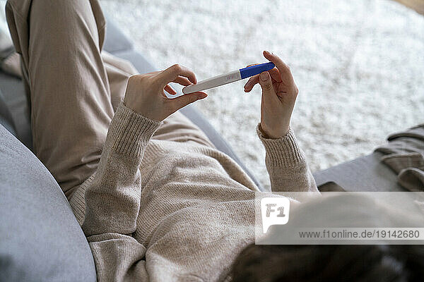 Woman holding pregnancy testing kit relaxing on sofa