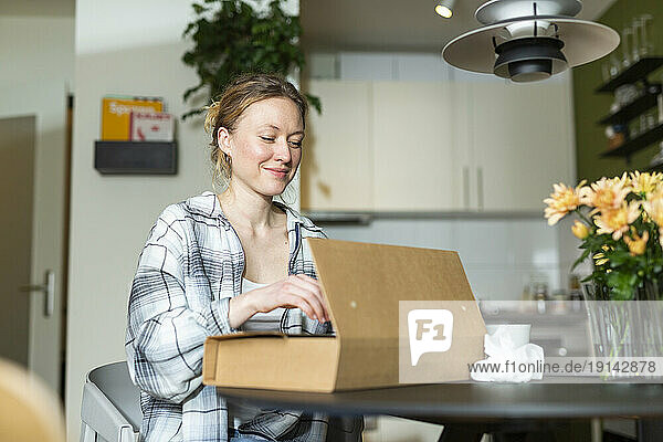 Smiling young woman unpacking cardboard box on table