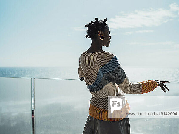 Young woman standing at glass railing enjoying fresh air