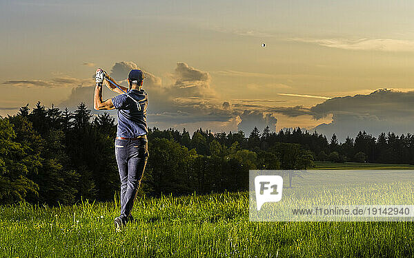 Young man playing golf standing on grass at dusk