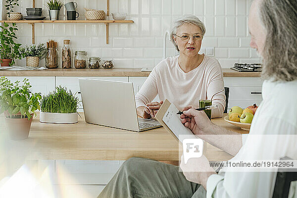 Mature nutritionist discussing with client preparing menu planner at home