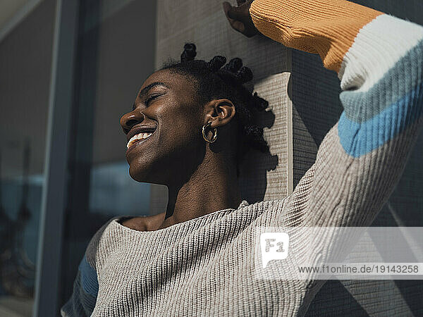 Smiling young woman enjoying sunlight on balcony