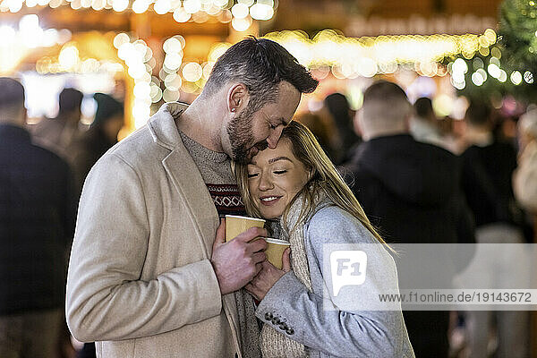 Loving couple hugging each other with coffee cup at Christmas market