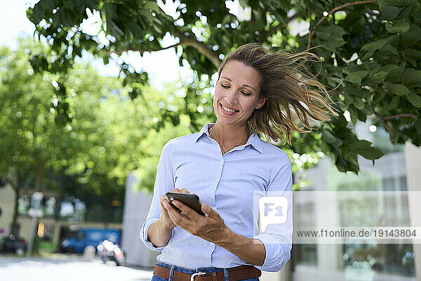 Smiling woman with tousled hair using smart phone
