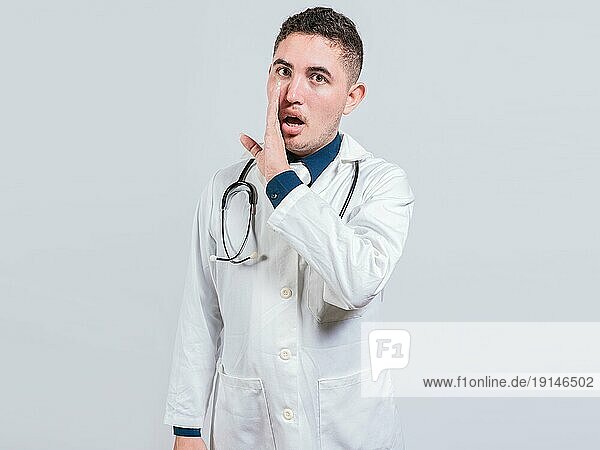Junger Arzt flüstert ein Geheimnis auf isoliertem Hintergrund. Handsome Arzt erzählt einen Klatsch isoliert  Arzt erzählt ein Geheimnis