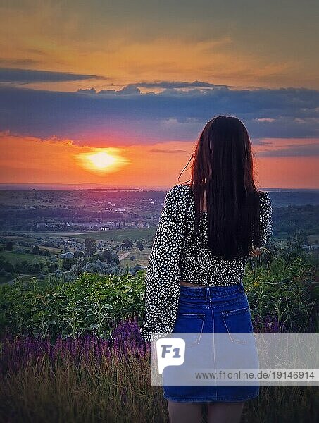 Rückansicht einer Frau im Rock  die den Sonnenuntergang über dem Tal beobachtet. Natürliche Sommerdämmerung Szene