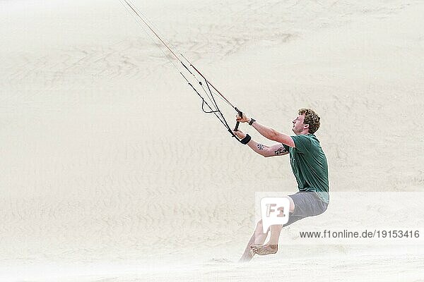 Junger Mann beim Umgang mit der 4 Leiner Bar eines fliegenden Vierleiner Trainers Parafoil  4 Leiner Lenkdrachen am Sandstrand bei starkem Wind im Sommer