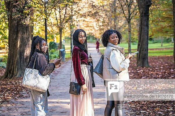 Drei multikulturelle Freunde drehen sich um und lächeln in die Kamera  als sie durch einen Park gehen