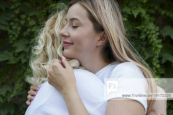 Smiling young woman hugging mother in front of plants