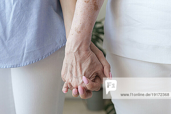 Young woman holding hands with mother at home
