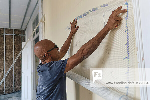 Mature construction worker measuring with mesh sheet on wall at site