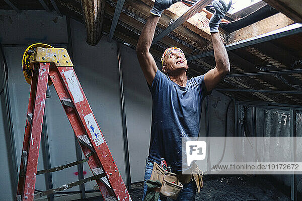 Mature construction worker repairing ceiling in attic