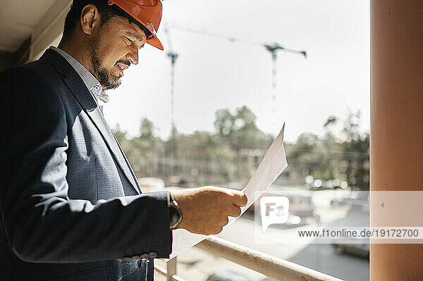 Engineer reading document in balcony on sunny day