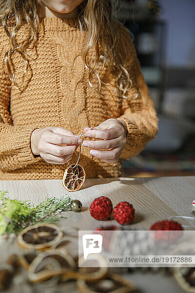 Girl making Christmas decoration from slice of dried lemon
